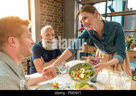 smiling woman serving homemade salad on plate during family dinner Stock Photo