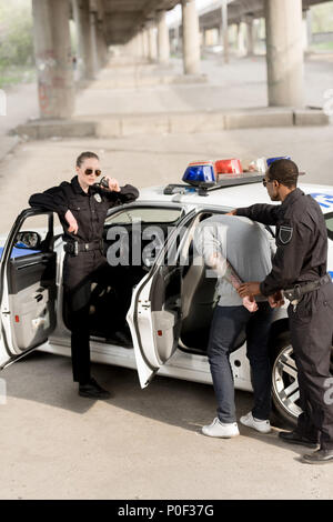 policewoman talking on portable radio while her partner holding criminal Stock Photo