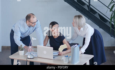 Beautiful business people are using laptop, studying documents, talking and smiling while working in office Stock Photo