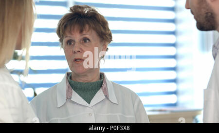 Older nurse having conversation with younger colleagues Stock Photo