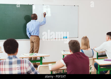 Rear view of high school students and teacher writing on white board in classroom Stock Photo