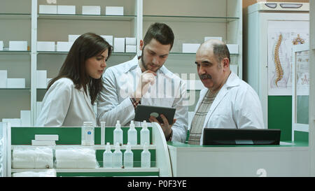 Three concentrated pharmacists using tablet computer at a counter in a pharmacy Stock Photo