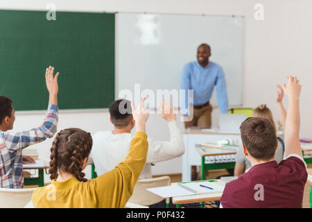 Rear view of high school students with arms up and african american teacher in classroom Stock Photo