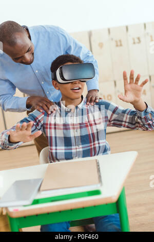 African american teacher holding shoulders of schoolboy using virtual reality headset Stock Photo