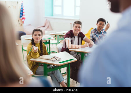 Cropped image of teacher with schoolgirl and classmates sitting at desks Stock Photo