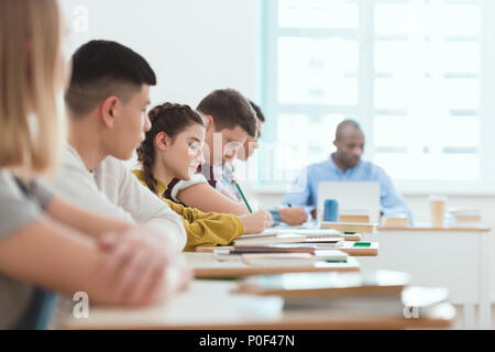 Side view of schoolchildren sitting in row and teacher at table with laptop in classroom during lesson Stock Photo