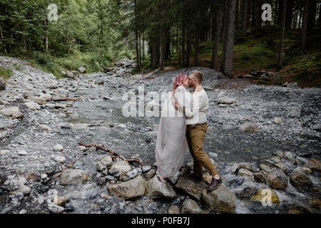 beautiful young wedding couple kissing while standing on rocks in rapid mountain river, Alps Stock Photo
