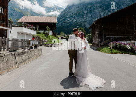 back view of couple hugging and kissing on road in town in Alps Stock Photo