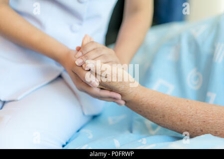 Nurse sitting on a hospital bed next to an older woman helping hands, care for the elderly concept Stock Photo
