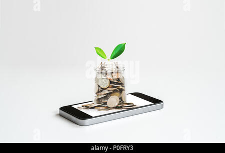 Online banking and making money by online business and e-commerce. Mobile phone and glass jar full of coins Stock Photo