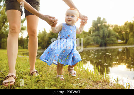 The baby with his mom takes the first steps in the park in the summer. Stock Photo