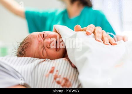 Newborn baby boy crying with hospital worker in the background Stock Photo