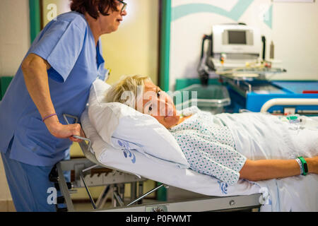 Young tired, but smiling woman on hospital bed transported through hospital corridor Stock Photo