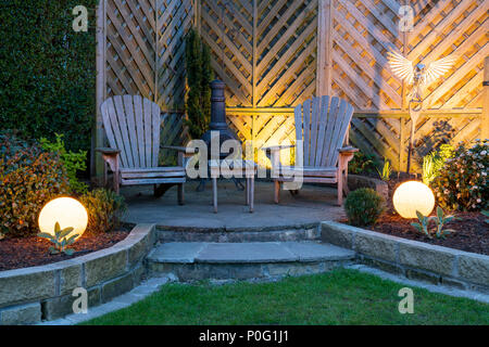 Beautiful, landscaped, private garden with contemporary design, borders & patio seating illuminated by globe lights at dusk - Yorkshire, England, UK. Stock Photo