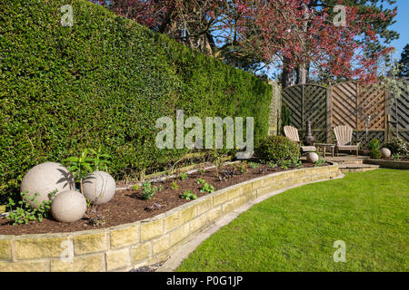 Sunny corner of beautiful, landscaped, private garden (contemporary design, border plants, patio seating, lawn & ornaments) - Yorkshire, England, UK. Stock Photo