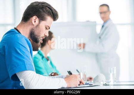 side view of handsome young doctor writing in clipboard while general practitioner making presentation Stock Photo