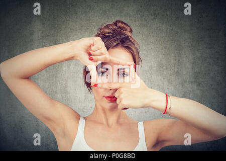 Young girl making frame with fingers and looking through limits at camera on gray background Stock Photo