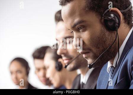 Close-up view of focused call center operator in headset working with colleagues behind Stock Photo