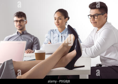 cropped shot of businesswoman sitting with legs on table while her colleagues working at office Stock Photo