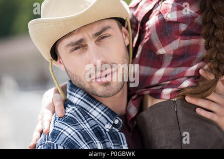 young handsome cowboy embracing his girlfriend and looking at camera Stock Photo