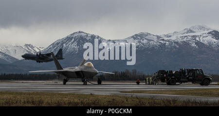 An F-22 Raptor refuels while a C-130 Hercules takes off at Joint Base Elmendorf-Richardson, Alaska, May 10, 2018. The Raptor performs both air-to-air and air-to-ground missions allowing full realization of operational concepts vital to the 21st century Air Force. The C-130 can accommodate a wide variety of oversized cargo, including utility helicopters and six-wheeled armored vehicles to standard palletized cargo and passengers. (U.S. Air Force photo by Senior Airman Curt Beach) Stock Photo