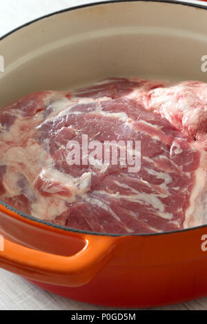 Raw shoulder of lamb in an orange ceramic roasting dish prepared to be cooked Stock Photo
