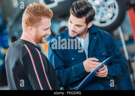 Young automechanic showing client a clipboard at a repair shop. Stock Photo