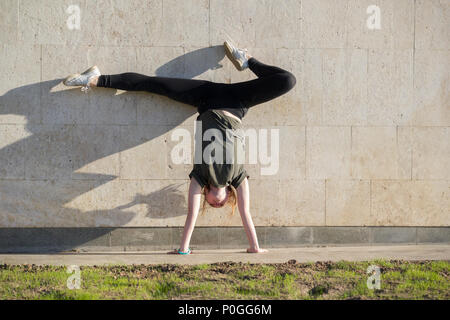 Young female handstand against the wall performs acrobatic elements Stock Photo