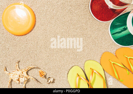 flat lay with flying disk, colorful caps, flip flops and seashells on sand Stock Photo