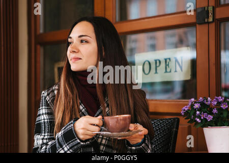Young beautiful girl drinks coffee or hot chocolate in a street cafe Stock Photo
