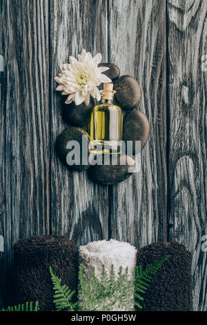 top view of arranged essential oil black pebbles with chrysanthemum flower  and towels for massage and spa on wooden surface Stock Photo