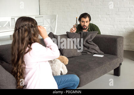 father and daughter with toy gun and binoculars playing together and looking at each other at home Stock Photo