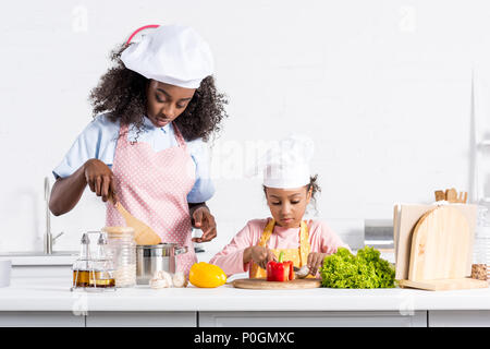 african american mother and daughter in chef hats cooking on kitchen Stock Photo