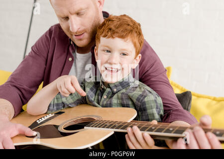 cropped shot of father teaching happy son playing guitar at home