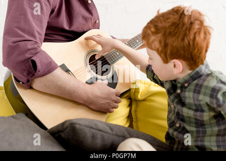 cropped shot of cute little boy looking at father playing guitar