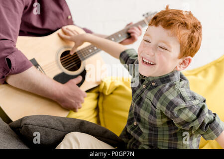 cropped shot of cute little boy laughing and father playing guitar