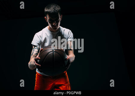 Man in prison uniform holding basketball ball on dark background Stock Photo