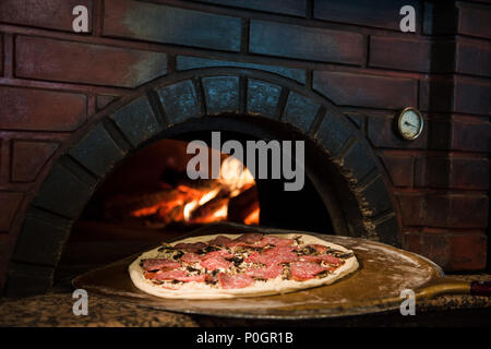 close up view of cooking process of raw pizza on wooden stove in brick oven Stock Photo
