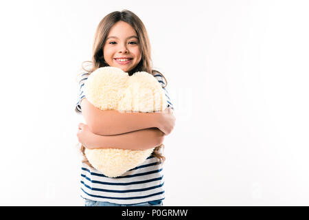 Smiling child hugging heart shaped pillow and looking at the camera isolated on white Stock Photo