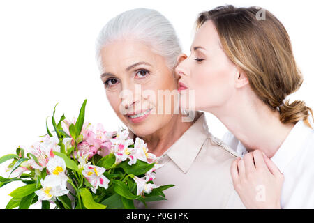 adult daughter kissing her mother with bouquet of flowers, isolated on white Stock Photo