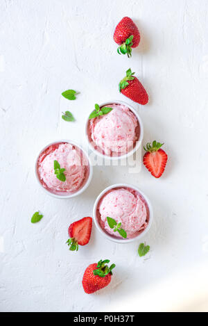 Strawberry ice cream and fresh strawberries on white background, top view. Three bowls of strawberry ice cream, healthy summer dessert. Stock Photo
