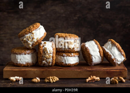 Ice cream sandwiches with nuts and wholegrain cookies. Homemade vanilla ice cream sandwiches on dark wooden background. Stock Photo