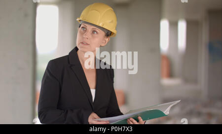 Female architect looking at blueprints at construction site Stock Photo