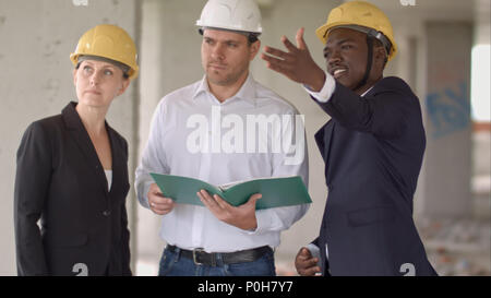 Group of smiling builders in hardhats with clipboard and blueprint outdoors Stock Photo