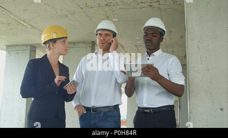 Executive team on construction site reviewing with tablet, smartphone, formal dressed people reading construction tablet Stock Photo
