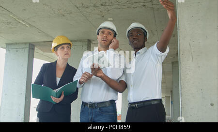 Executive team on construction site discussing project, using smartpone and digital tablet Stock Photo