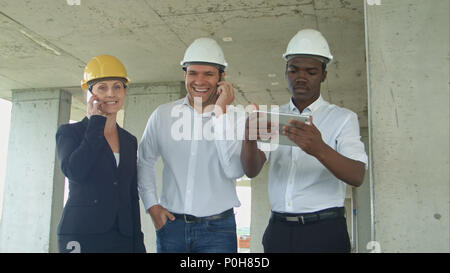 Executive team on construction site discussing project, using tablet, having phone calls with smartphone Stock Photo