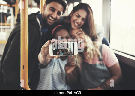 Smiling group of diverse young friends taking selfies together while riding on a bus Stock Photo