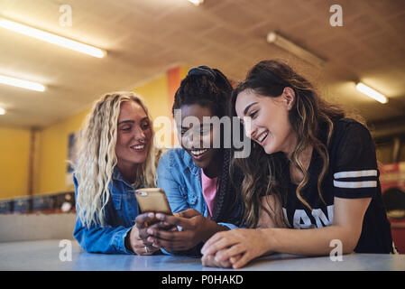 Smiling young female friends leaning on the counter of a laundromat using a cellphone while doing laundry together Stock Photo