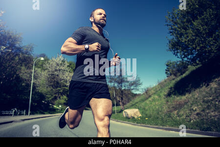 Fit young man in sportswear listening to music on earphones while running alone along a country road Stock Photo